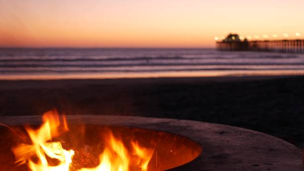 campfire pit in california usa. camp fire on twilight ocean beach, bonfire flame by sea water waves. - bonfire beach fire barbecue imagens e fotografias de stock