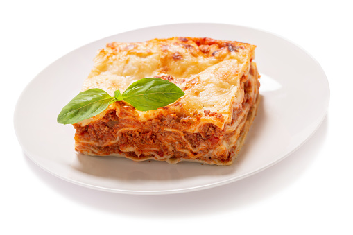 plate of lasagna with green basil isolated on white background