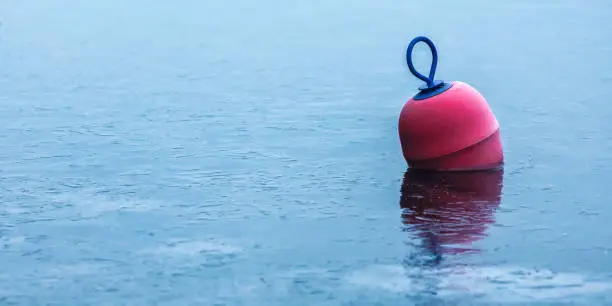 A red buoy frozen in ice in a winter water surface.