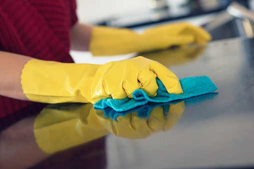 A person standing at a kitchen counter and wiping it clean with a dish cloth.