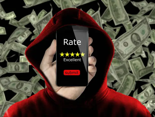 Photo of anonymous with hoodie making fake rating and review for money concept conceptual. Untrue feedback in exchange of dollars. Business online ranking is affected from false review by user to gain money.