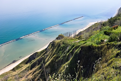 Panoramic view of cliffs of the rugged coastline with breakwaters protecting the beach of Fiorenzuola di Focara (Pesaro, Marche, Italy)