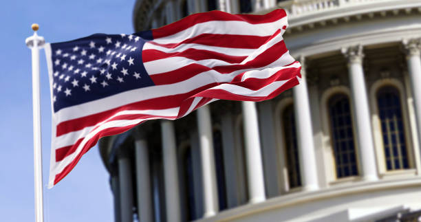 the flag of the united states of america flying in front of the capitol building blurred in the background - eua imagens e fotografias de stock