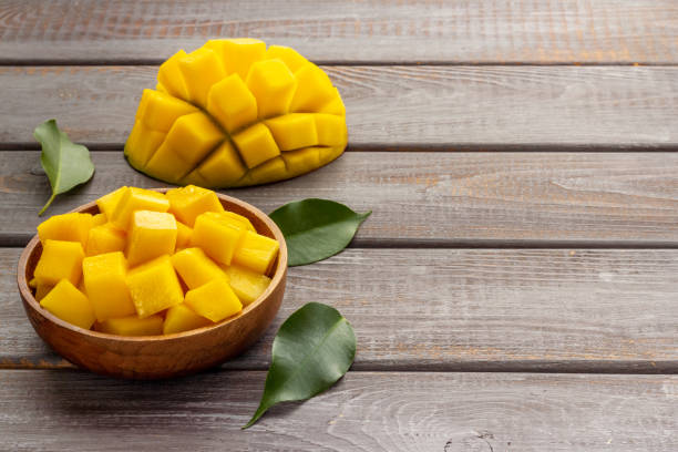 Mango fruit slices and cubes in wooden bowl stock photo
