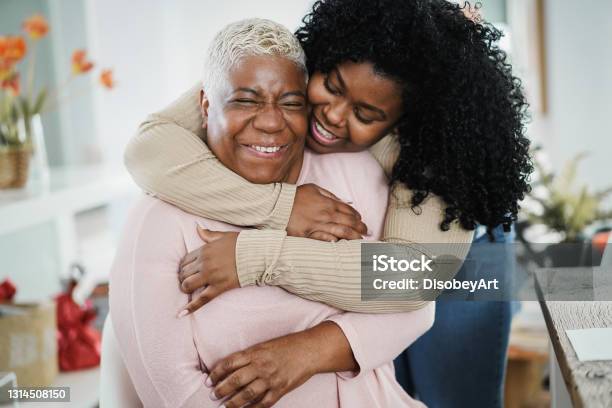 African Daughter Hugging Her Mum Indoors At Home Main Focus On Senior Woman Face Stock Photo - Download Image Now