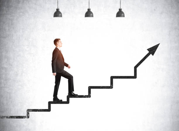 istock Businessman going up on stairs on grey concrete background with lamps 1314511541