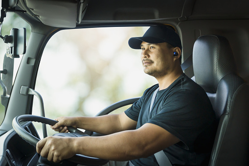 Professional male truck driver Asian driving transport vehicle and fastening seat belt safety. men trucker confident smile and look navigation device. concept Courier man, Transportation, delivery