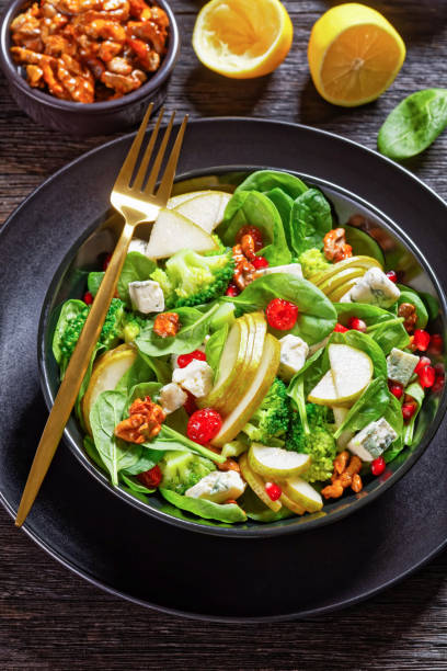 istock pear salad with blue cheese cubes, broccoli, spinach leaves, caramelized walnuts and pomegranate seeds  on a black plate on a wooden table, vertical view from above 1314511841