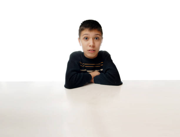 istock Surprised young boy sitting at a huge table against white background 1314512939