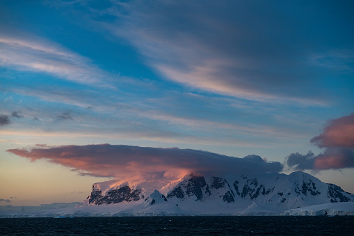 Late-evening sun strikes clouds and a snow-covered island under partly cloudy skies, Near Base Brown, Paradise Bay, Graham Land, Antarctic Peninsula, Antarctica