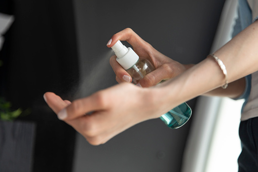 Unrecognizable woman preventing covid-19 by spraying her hands with disinfecting hand sanitizer.