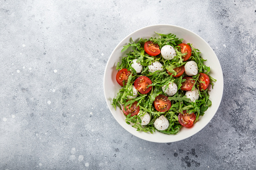 Mozarella, tomato and arugula salad in whute bowl, topview, copy space