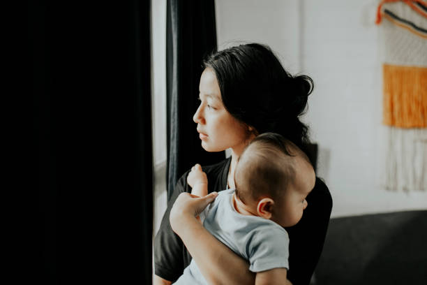Young woman carrying baby looking throughout window Young woman carrying baby looking throughout window postpartum depression stock pictures, royalty-free photos & images