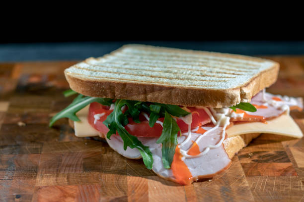 istock Sandwich with ham, arugula, cheese and tomato on a cutting board. In a dark key. Selective focus. 1314525780