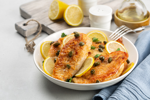 Chicken piccata on white table. Chicken breast dredged in flour and cooked in sauce cantaining lemon juice, butter and capers.