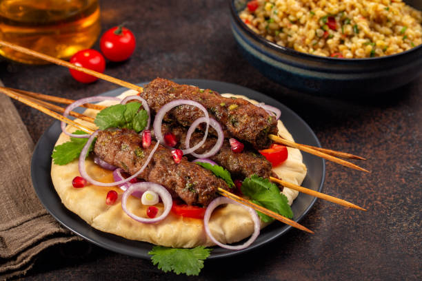 istock Dinner woth homemade beef Kofta kebabs with coriander on pita bread with red onion, tomatoes and pomegranate seeds. Bulgur salad on background. Dark brown table. 1314526394