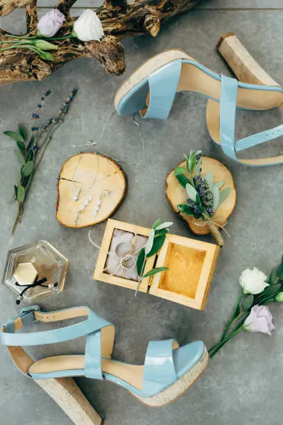 Photo of Wedding rings lie in a wooden box surrounded by sandals with heels, flowers and twigs on the floor