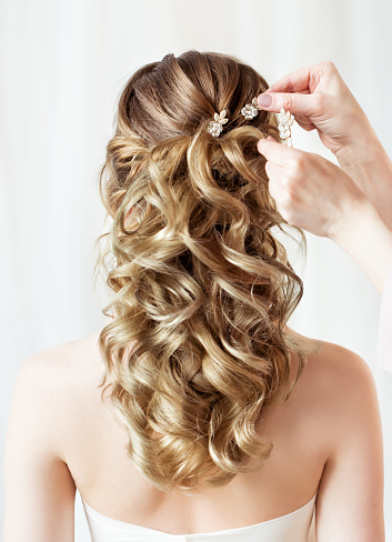 Wedding Hair Style Back Side View Close up. Bride Hairstyle Accessory Rear View Close up. Hairdresser hands putting Flower Crystal Hairpin. Wavy curl Evening Hairdo over White Background