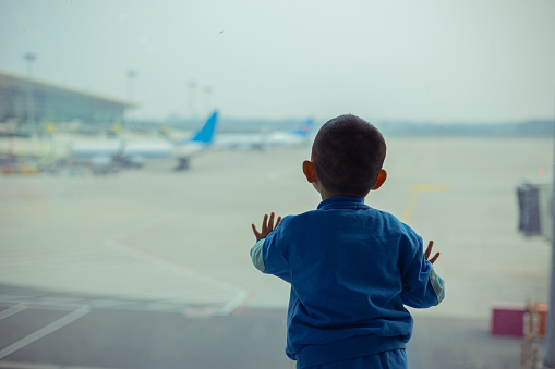 Little baby boy standing in airport looking out of window waiting flight.