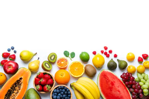 Overhead view of multicolored fresh ripe organic fruits shot on white background. The composition is at the bottom of an horizontal frame leaving useful copy space for text and/or logo and includes mango, orange, strawberry, blueberry, kiwi, peach, grape, watermelon, banana, papaya, apple, pear, fig, lime and lemon. High resolution 42Mp studio digital capture taken with SONY A7rII and Zeiss Batis 40mm F2.0 CF lens