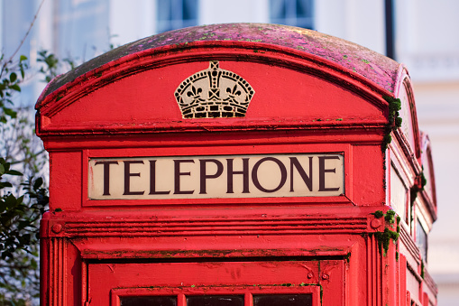 Vintage red telephone box close-up. Word telephone from iconic street box London UK. Retro image of old telephone box roof top.