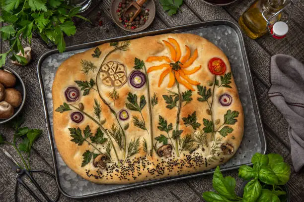 Floral painting focaccia,  garden flatbread art, food trend. Old wooden background, top view