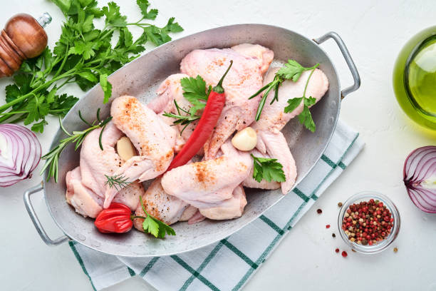 istock Raw chicken wings in a white bowl with spices and ingredients for cooking on light slate, stone or concrete background. Top view with copy space. Mock up. 1314543714