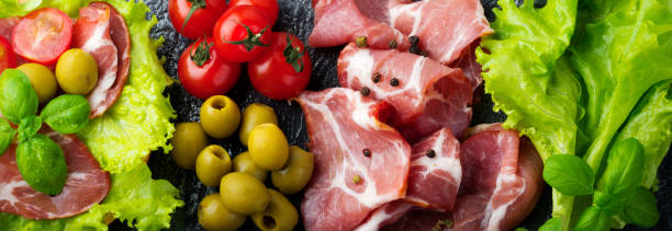istock Sandwich with dried meat, jamon with cherry tomatoes, basil, ciabatta, olives on a black background. Selective focus.Top view. Copy space 1314544832