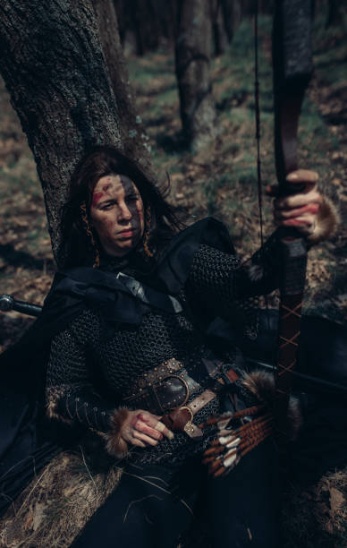 istock Woman in image of medieval warrior sits and rests in forest. 1314544852