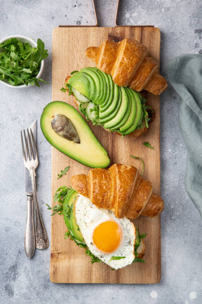 croissant sandwich with avocado, fried egg and arugula for breakfast
