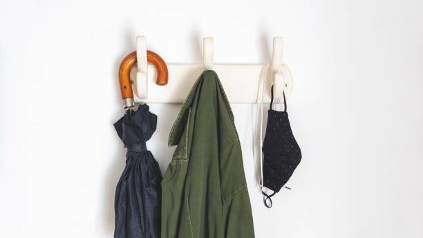 new normal things you need if you are going outside in the new normal because of covid-19. Hanging from a coat rack an umbrella, a coat, face masks and headphones. Over a white wall. Taken inddor with natural daylight coat hook photos stock pictures, royalty-free photos & images