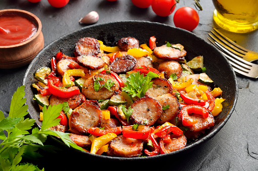 Slices of fried sausages with vegetables and spices in frying pan, close up view