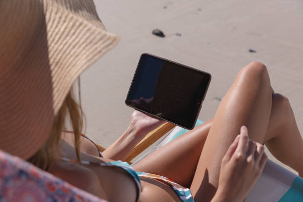 istock Mid section of caucasian woman using digital tablet while sitting on deck chair at the beach 1314551810
