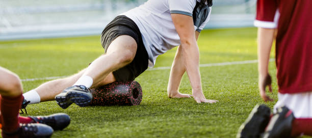istock Football physiotherapist personal trainer using foam roller. Trainer showing exercises to kids soccer players in a team. Football stretching session in school team 1314552005