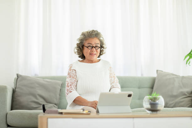 istock Happiness elderly asian woman with white hairs sitting on sofa and using computer tablet VDO Conference online meeting with family and smile at home,Senior lifestyle at home concept 1314559535