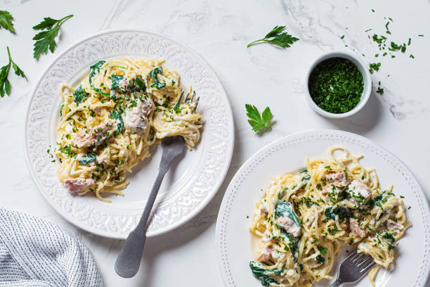 istock Spaghetti pasta with tuna, spinach and creamy sauce on white plate with fresh herbs, white marble background. 1314565043