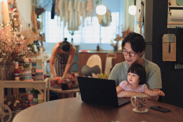 Asian business man working from home with his wife and child in the background stock photo