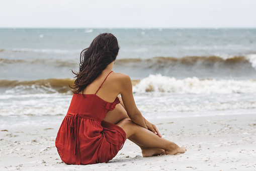 Woman in red dress sitting on cold windy beach