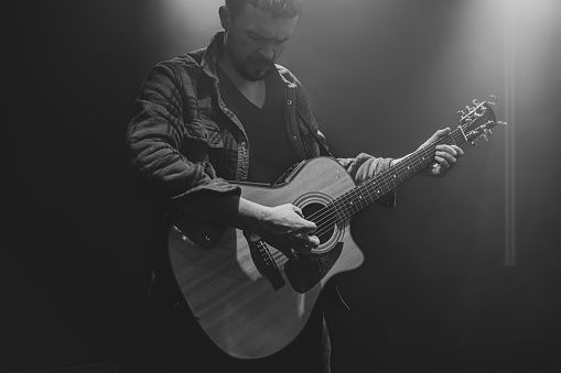A man plays an acoustic guitar at a partially lit concert.