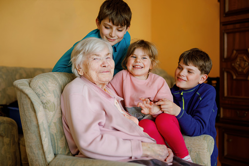 Great-grandmother with three children, siblings. Family of four, two boys and little toddler girl. Happy senior old woman and grandchildren, indoors