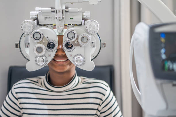 Close-up Of african teen girl Doing Eye Test On Phoropter, African teen girl checking on her eye with optometry machine. Close-up Of african teen girl Doing Eye Test On Phoropter, African teen girl checking on her eye with optometry machine. eye test equipment stock pictures, royalty-free photos & images