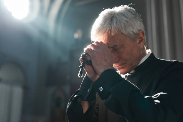 Priest praying in the church Senior priest holding rosary beads praying while sitting in the church clergy stock pictures, royalty-free photos & images