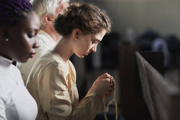 Woman praying in the church Young woman holding rosary while praying in the church among other people catholicism stock pictures, royalty-free photos & images