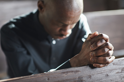 African man sitting with eyes closed and praying in the church