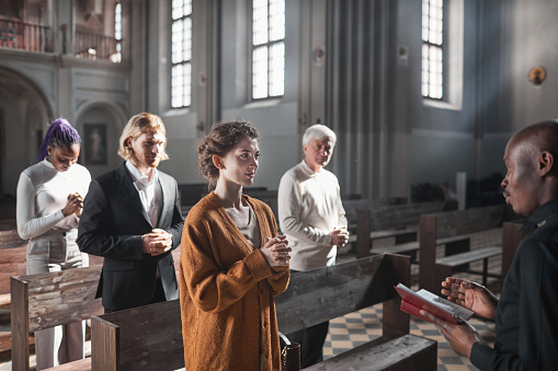Group of people standing and listening the pray while priest reading it in the church