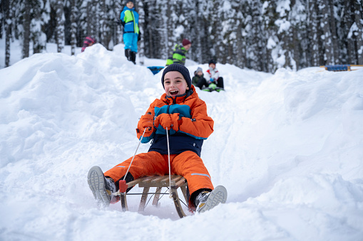 Smiling boy enjoying tobogganing on snowy landscape.