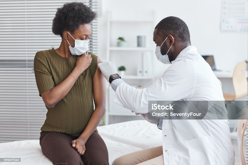 Doctor vaccinating he patient African doctor in white coat vaccinating pregnant woman during her visit at hospital Vaccination Stock Photo