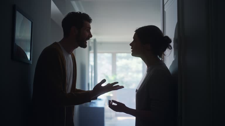 Young Couple Arguing and Fighting. Domestic Violence and Emotional abuse Scene, Stressed Woman and aggressive Man Screaming at Each other in the Dark Hallway of Apartment. Dramatic Scene