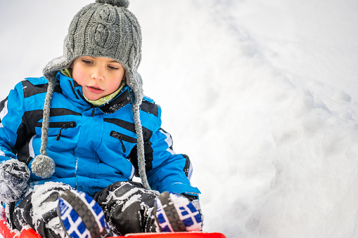 Boy enjoying tobogganing on snowy hill during winter.