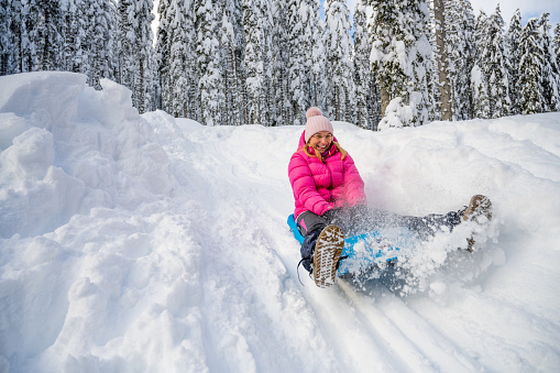 Smiling woman enjoying tobogganing on snowy hill during winter.